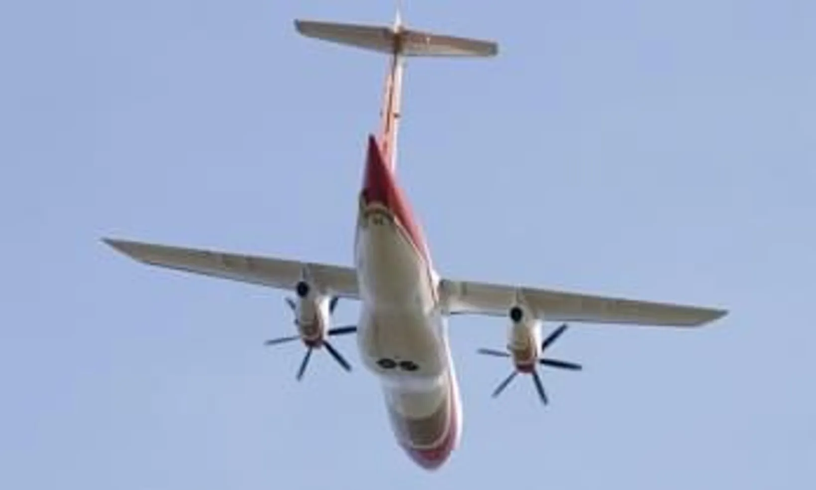 Fairchild Dornier 328 twin-engine aircraft in flight, photographed from below against clear blue sky, showing red and whit...