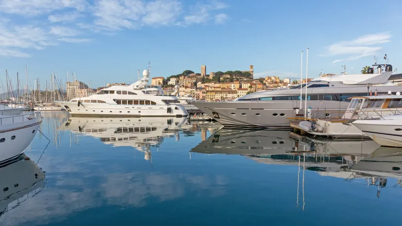 Yacht di lusso attraccati in un porto turistico di Cannes, con la pittoresca città e l'architettura storica sullo sfondo. Cannes è rinomata per il suo stile di vita glamour e gli eventi prestigiosi.