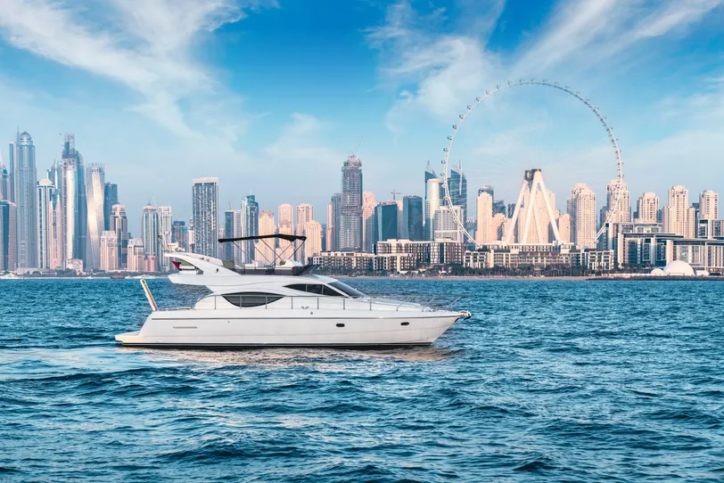 Egy luxusjacht Dubai látképének lenyűgöző hátterében, ikonikus felhőkarcolókkal és az Ain Dubai kilátókerékkel.