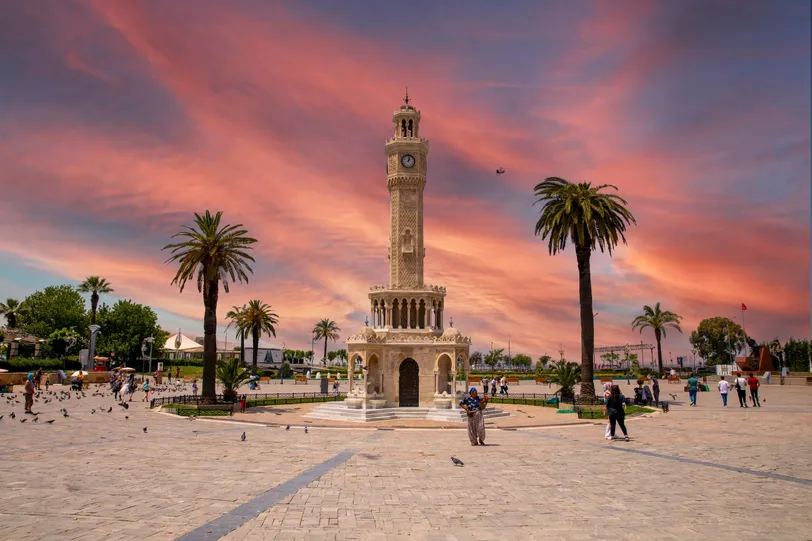 L'iconica Torre dell'Orologio in Piazza Konak, a Izmir, splendidamente illuminata sotto un tramonto drammatico, rappresenta il cuore della vita frenetica e il significato storico della città.