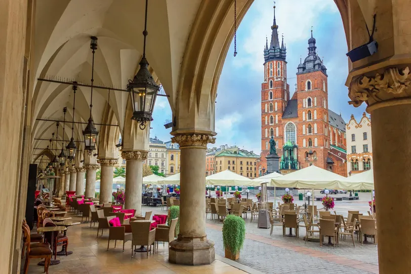 Una vista pittoresca della Piazza del Mercato Principale di Cracovia, che mette in mostra lo storico Palazzo dei Tessuti e la Basilica di Santa Maria con caffè all'aperto.