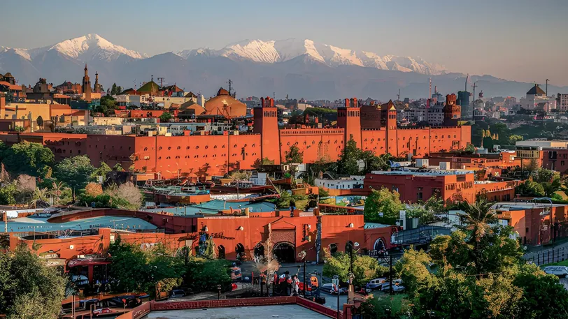 El paisaje urbano de Marrakech con las montañas del Atlas de fondo, capturando los colores vibrantes y la arquitectura única de la ciudad.