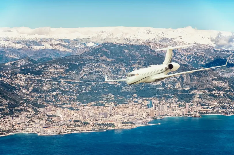 Un jet privato che sorvola Monaco, mostrando la splendida costa mediterranea e lo sfondo montuoso, evidenziando Monaco come una destinazione di lusso per l'aviazione privata.