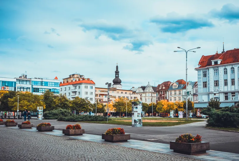 Une vue de la place Masaryk à Ostrava, mettant en valeur le mélange d'architecture moderne et historique avec des jardinières de fleurs vibrantes bordant le chemin.
