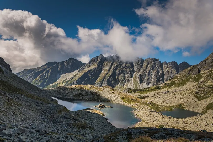 Tatry Wysokie w pobliżu Popradu na Słowacji mają urwiste szczyty i spokojne alpejskie jeziora pod częściowo zachmurzonym niebem, oferując zapierającą dech w piersiach naturalną scenerię.