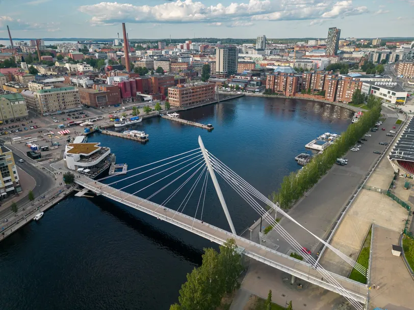 Malowniczy widok z lotu ptaka na Tampere w Finlandii, z nowoczesną infrastrukturą miasta, mostami i spokojnymi drogami wodnymi pod częściowo zachmurzonym niebem.