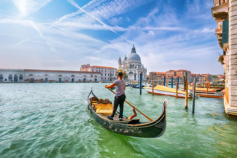 A velencei Canal Grande csatornán navigáló gondolás, a háttérben a Santa Maria della Salute-tal.