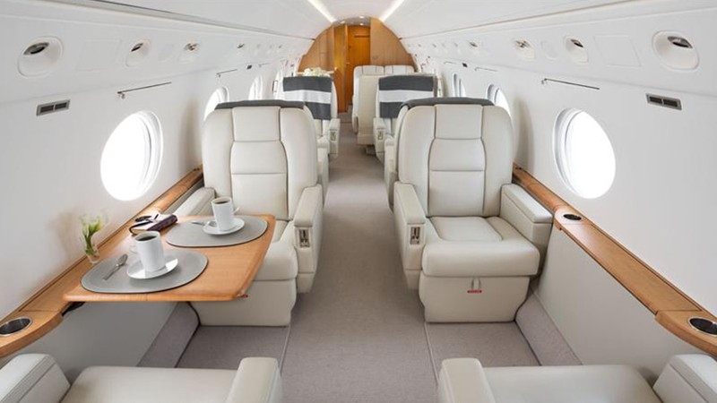 Gulfstream GV cabin interior featuring cream leather seats, wooden side tables with place settings, large windows, and coc...