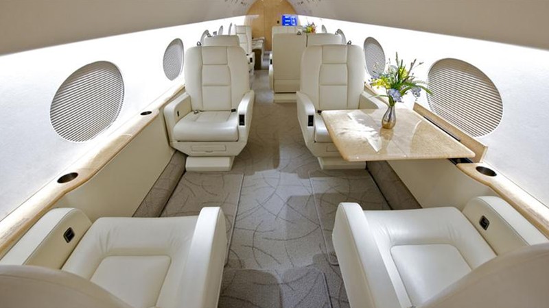 Gulfstream GV cabin interior overhead view showing cream leather seating, oval windows, carpeted aisle, and fresh flowers ...