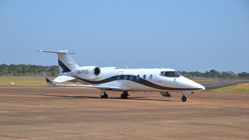 White Hawker 400XP private jet parked on tarmac, side view, with blue sky and green landscape background.
