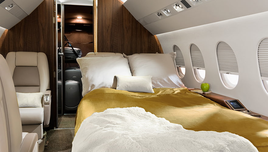 Luxurious cabin interior of Dassault Falcon 2000LX private jet featuring a bed with gold blanket, white pillows, windows, ...