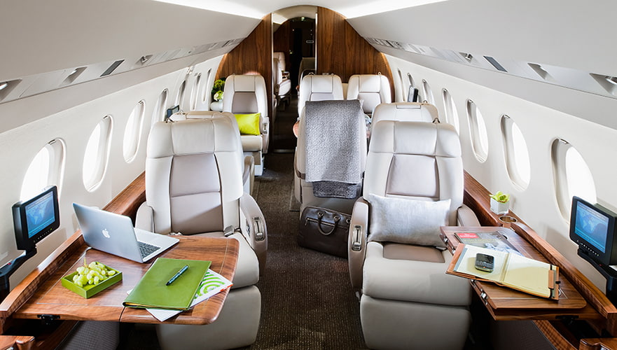 Dassault Falcon 2000LX cabin interior view showing luxurious seating, wooden accents, workstations with laptops, and oval ...