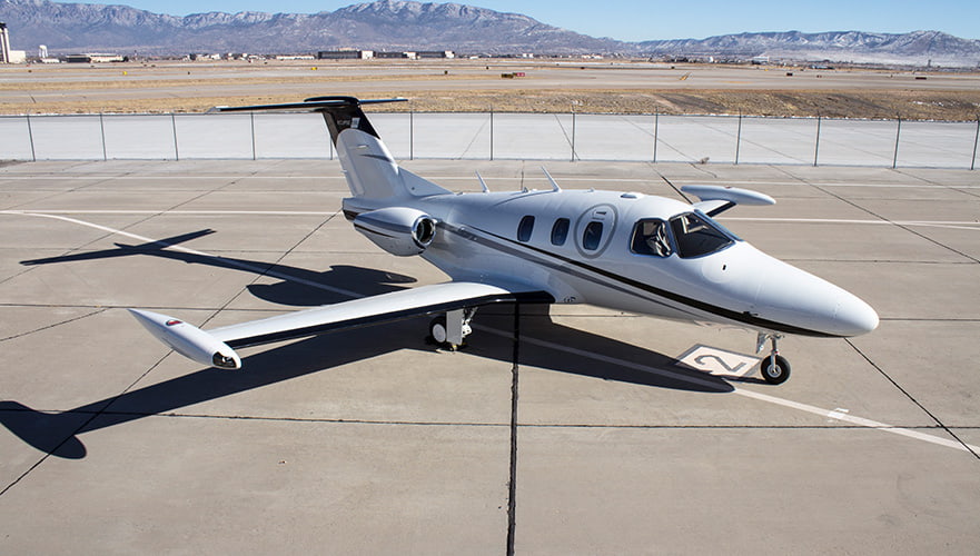 Eclipse Aerospace Eclipse 550 twin-engine jet parked on airport tarmac with mountains in background, side view.