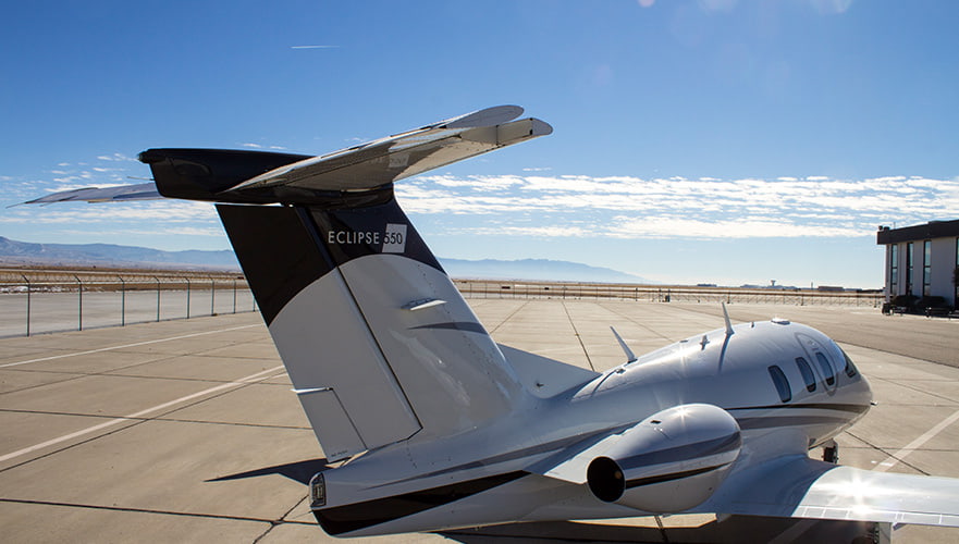 Eclipse 550 twin-engine jet parked on airport tarmac, rear quarter view showing distinctive split-scimitar winglets and sl...