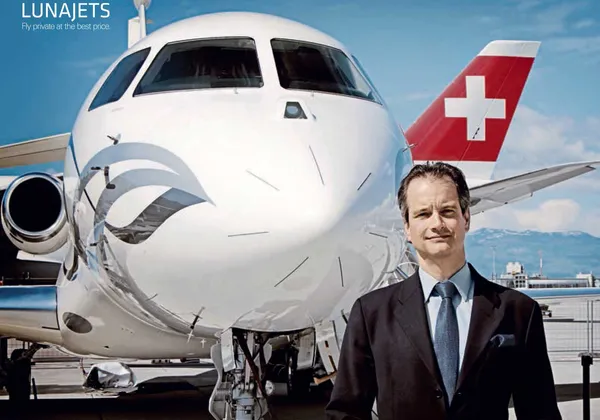 Mężczyzna w szarym garniturze i kapeluszu zmierzający w stronę prywatnego odrzutowca o zachodzie słońca