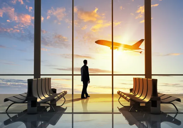 Sylwetka podróżnika w poczekalni na lotnisku, obserwującego start samolotu o wschodzie słońca
