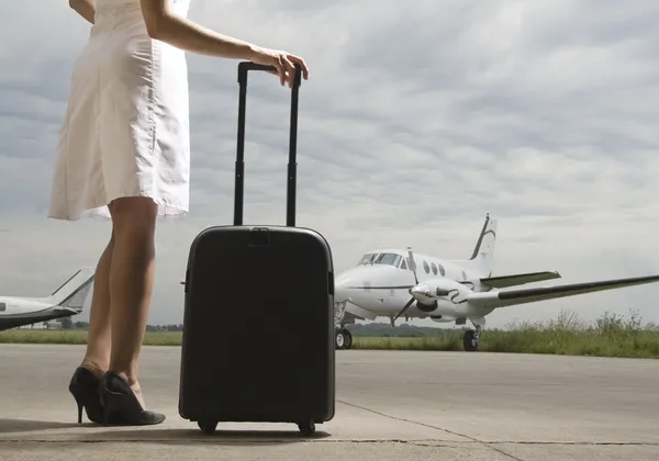Nő gurulós bőrönddel egy kis, kétmotoros magánrepülőgép felé sétál a repülőtér betonján