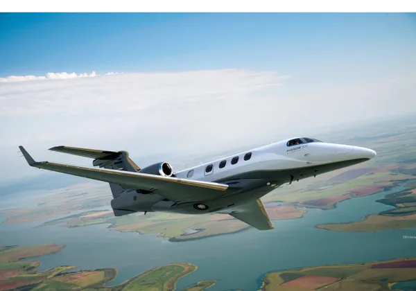 Samolot biznesowy Embraer Phenom 300 przelatuje nad jeziorem i polami uprawnymi