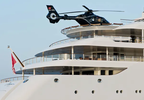 Czarny helikopter lądujący na górnym pokładzie lądowiska dla helikopterów luksusowego białego superjachtu