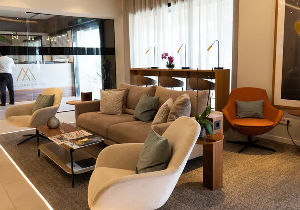 Nowoczesny salon FBO z beżowymi sofami, pomarańczowym krzesłem, stolikiem kawowym i storczykami przy recepcji