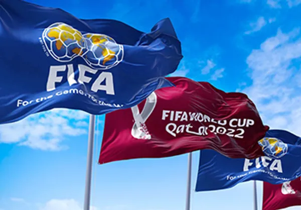 Niebieskie i czerwone flagi Mistrzostw Świata FIFA w Katarze 2022 powiewające na tle jasnoniebieskiego nieba