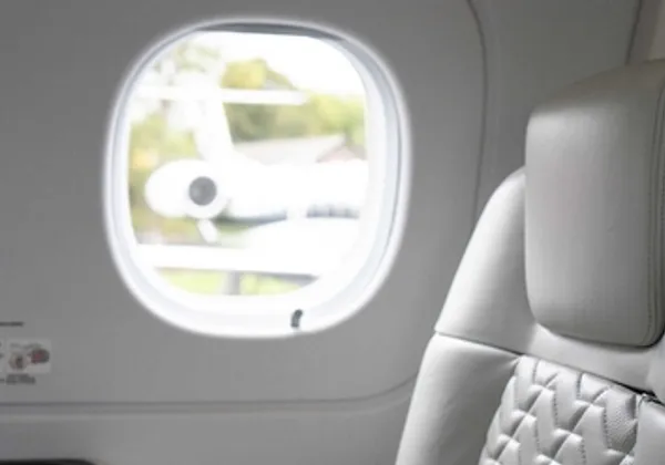 Zbliżenie na białe skórzane siedzenie i owalne okno wewnątrz prywatnego odrzutowca