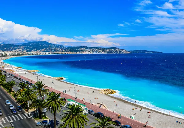Palmengesäumte Promenade entlang der türkisfarbenen Küste und des Strandes von Nizza an einem sonnigen Tag