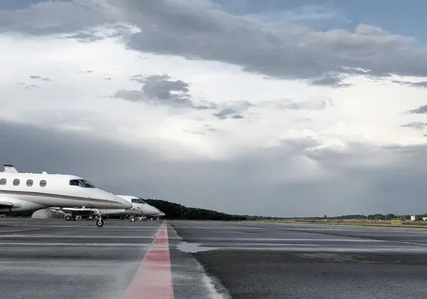 Rząd lekkich prywatnych odrzutowców zaparkowanych na mokrym pasie startowym pod zachmurzonym niebem
