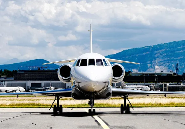 Biały prywatny odrzutowiec zaparkowany na pasie startowym z górami i niebem w tle
