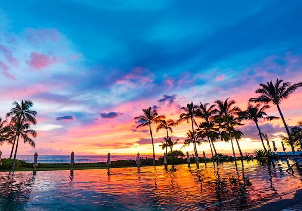 Zachód słońca nad spokojną hawajską plażą ze złotymi chmurami, turkusową wodą i bujnymi drzewami
