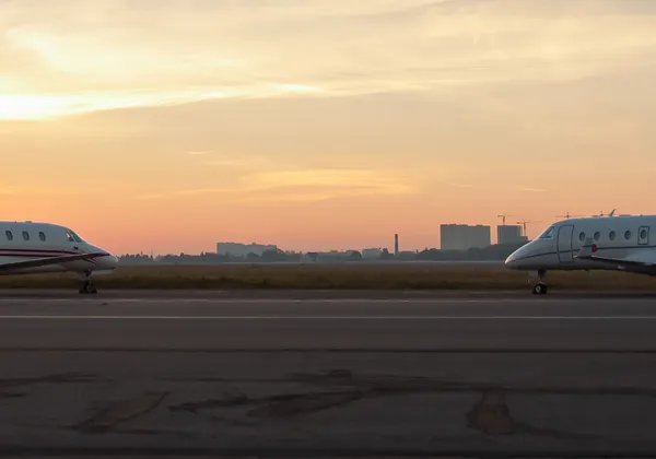 Dwa prywatne odrzutowce ustawione naprzeciwko siebie na pasie startowym o zachodzie słońca i na tle panoramy miasta