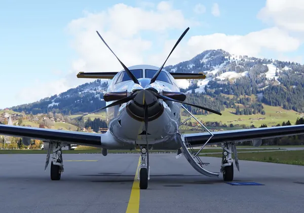 Samolot Pilatus PC‑12 zaparkowany na zaśnieżonym lotnisku Gstaad, z górami w tle