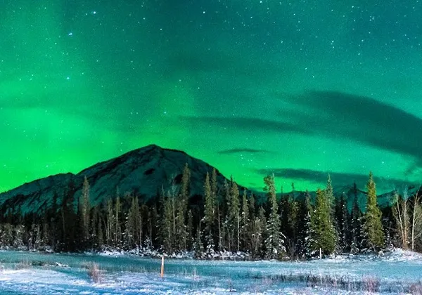 Sarki fény által megvilágított havas hegyi út és erdő éjszaka