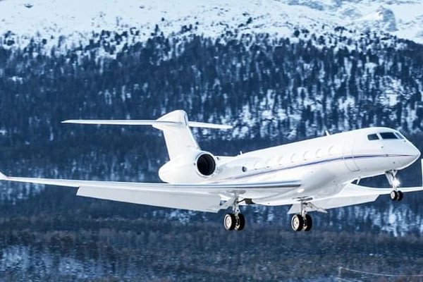 White private jet landing against a backdrop of snowy alpine mountains and forests