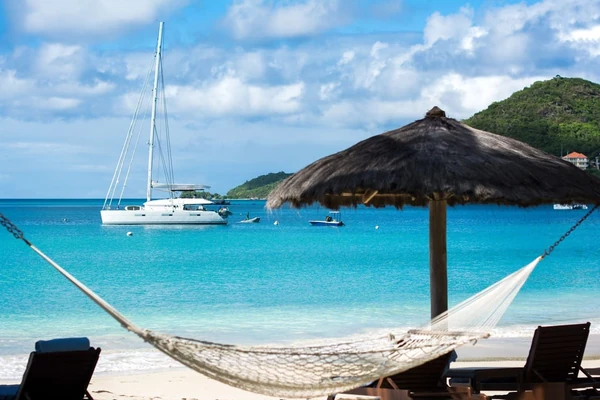 Hamac sur l'île de Canouan sous un parasol en chaume près de la baie turquoise et des collines