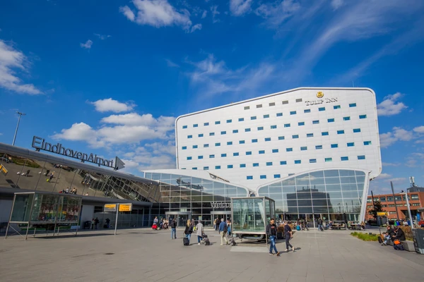 Terminal del aeropuerto de Eindhoven con arquitectura curva blanca moderna y horizonte de la ciudad bajo cielo azul