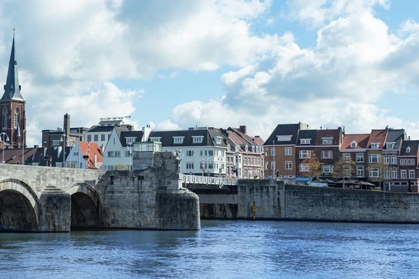 Paisaje urbano de Maastricht con puente de piedra histórico sobre el río Mosa y edificios coloridos a orillas del agua, Países Bajos