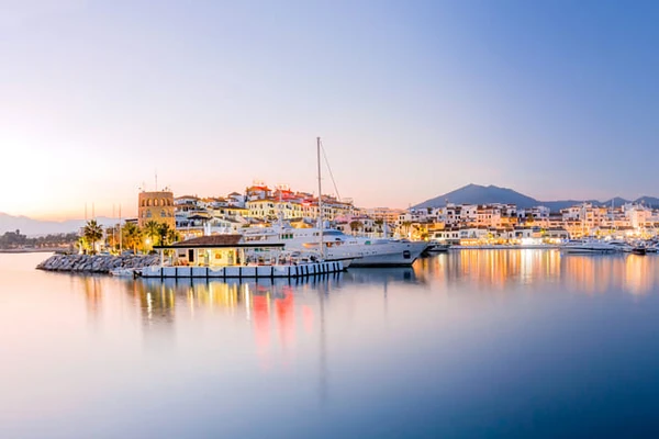 Serene harbor at sunrise with luxury yacht docked beside colorful Mediterranean waterfront buildings and mountain backdrop