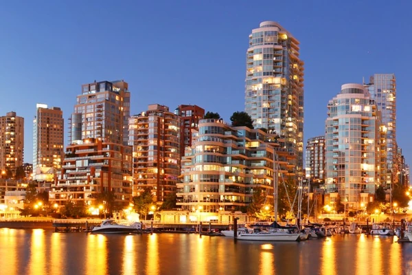 Photo de la ville de Vancouver la nuit avec ses gratte-ciel illuminés à l'arrière, et une rivière avec des bateaux à l'avant.