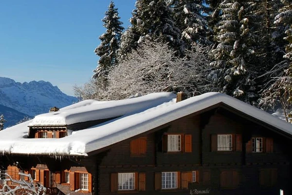 A la derecha hay un chalet con techo cubierto de nieve, a lo lejos a la izquierda están las montañas. Villars, Suiza.