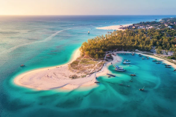 Vista aerea di un'isola tropicale con acque turchesi, spiagge di sabbia bianca, barche ancorate e lussureggiante vegetazione forestale al tramonto