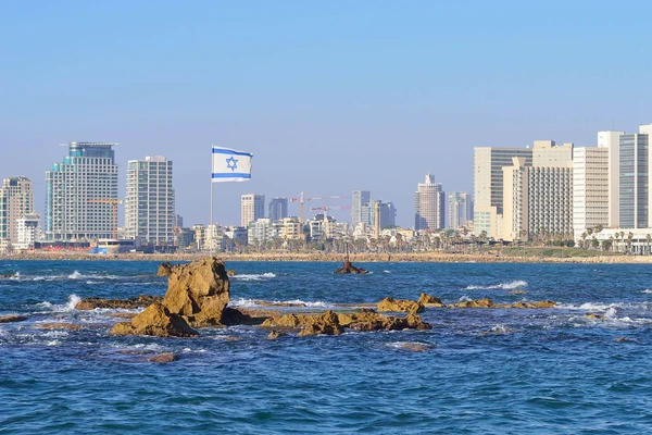 Die Flagge Israels, die vor dem Hintergrund der modernen Skyline von Tel Aviv weht