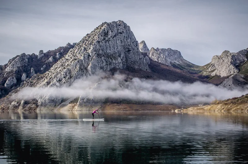 Egy lány vagy nő rózsaszín kabátban evezik egy ködös hegyi tavon