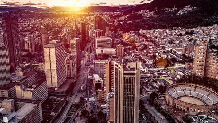 A kolumbiai Bogotá légi látképe naplementekor, magas irodatornyokkal, sűrűn beépített városrészekkel és a Santamaría bikaviadal-arénával.