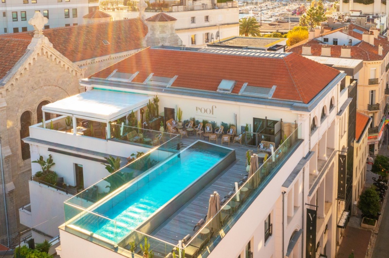 A Five Seas Hotel Cannes tetőtéri kilátása üvegfalú úszómedencével, napozóágyakkal és a város háztetőire nyíló panorámás kilátással.