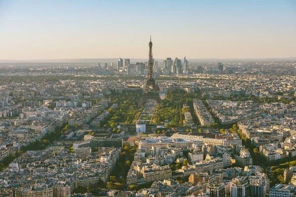 Aerial view of Paris, featuring the Eiffel Tower amidst the expansive cityscape, with the modern skyline of La Défense in the background