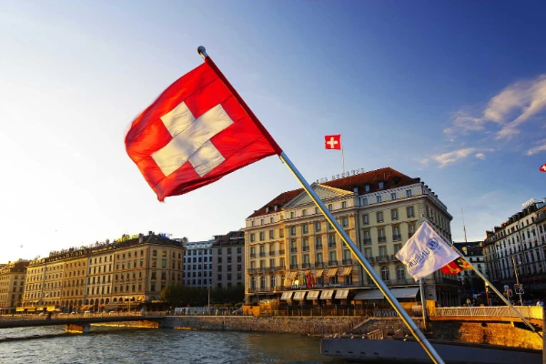Swiss flag waving prominently by the riverside buildings in Geneva