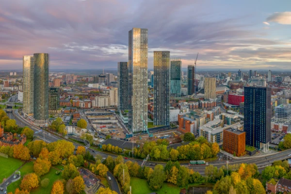 Вид сверху на городской пейзаж Манчестера на закате, на котором видны высотные здания и городская планировка.