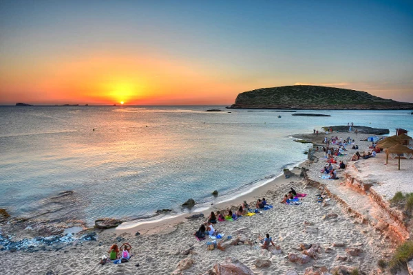 Ibizai strand naplementekor, emberek pihennek a homokban