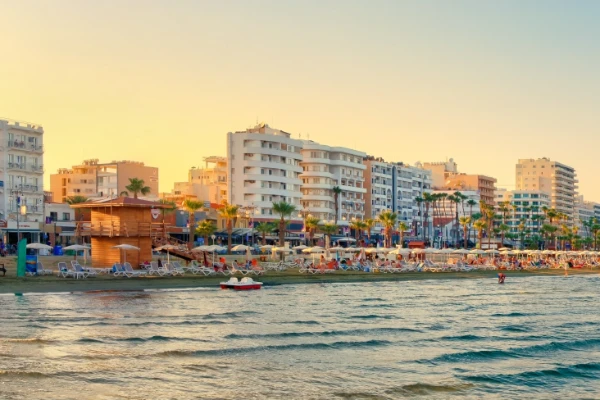 Dzielnica Foinikoudes w Larnace na Cyprze, z piaszczystą plażą, promenadą otoczoną palmami, nowoczesnymi budynkami i widokiem na Morze Śródziemne o zachodzie słońca